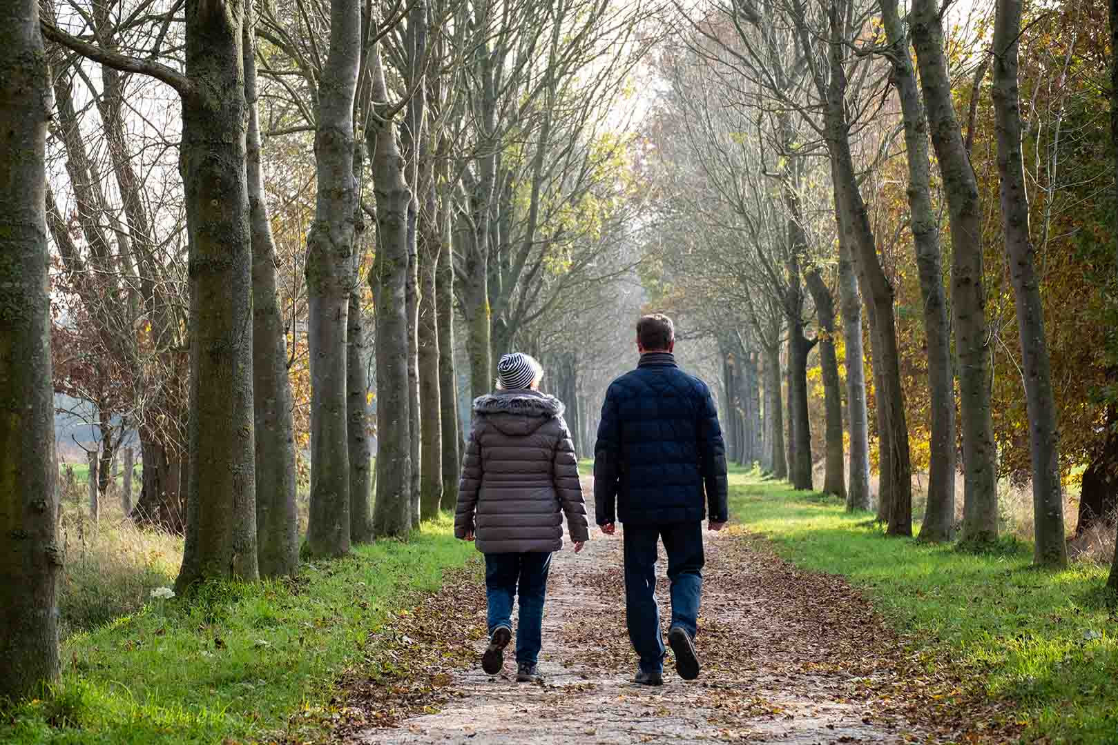 Ein Paar spaziert durch eine herbstliche Allee und geniesst die gemeinsame Zeit in der Natur.