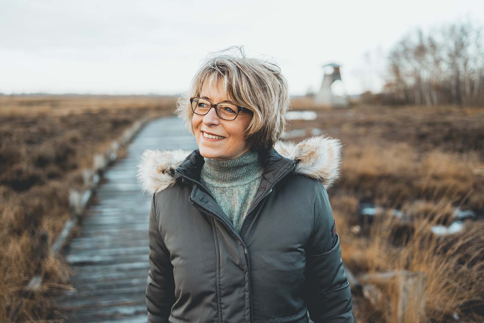 Eine Frau geniesst die frische Luft bei einem Spaziergang durch eine herbstliche Landschaft.