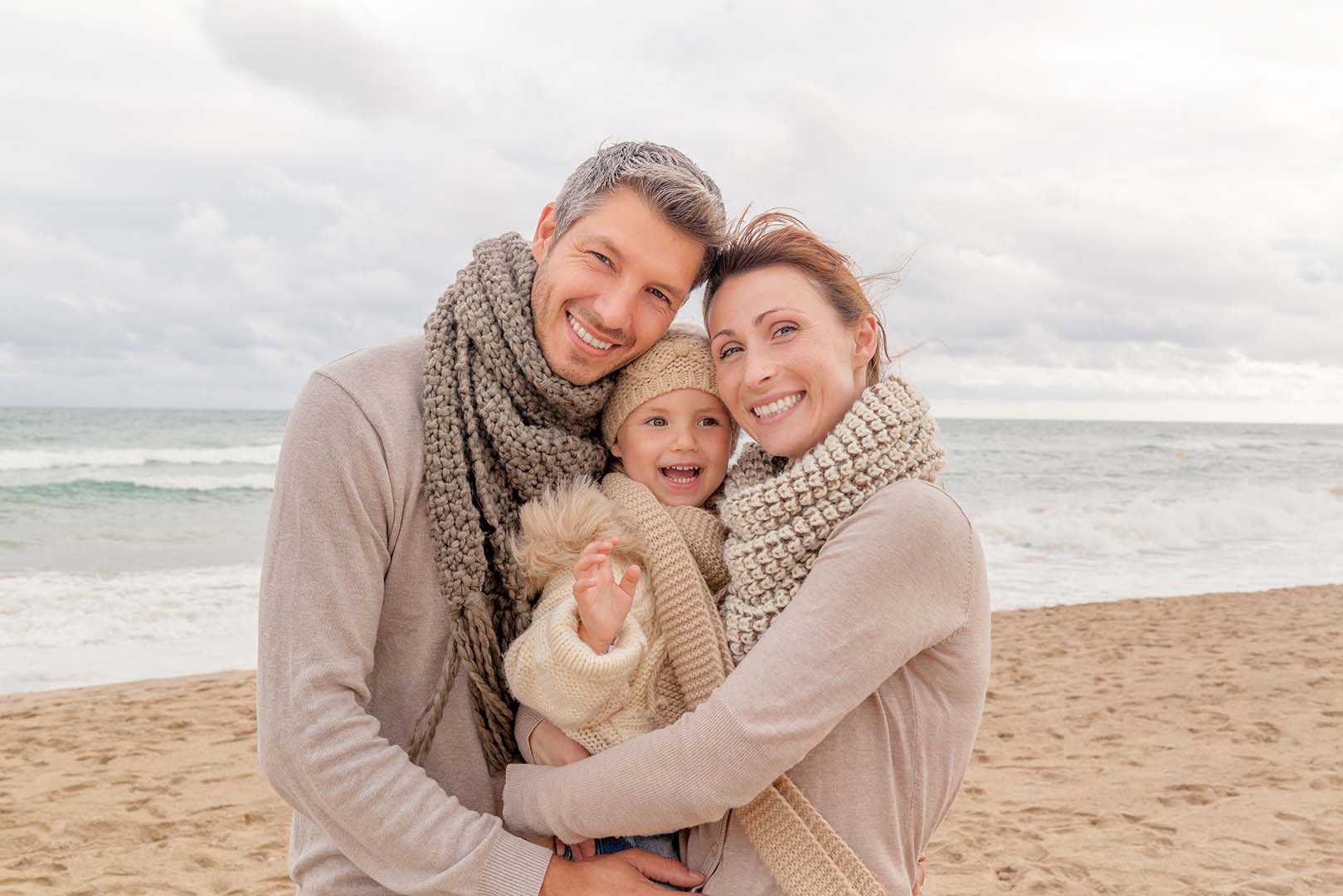 Eine junge Familie in warmer Kleidung geniesst einen gemeinsamen Moment am Strand.